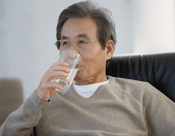 Pensive man drinking a glass of water on couch - Hydration