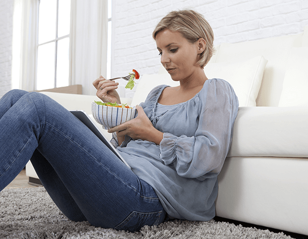 Woman sitting on the ground eating a bowl of fruit - IBS IBD