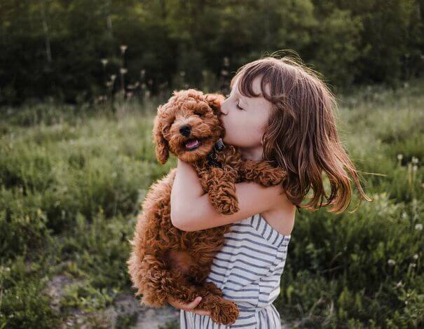 Child girl hugging and kissing a puppy outdoors